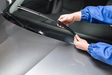 Technician is changing windscreen wipers on a car station. - obrazy, fototapety, plakaty