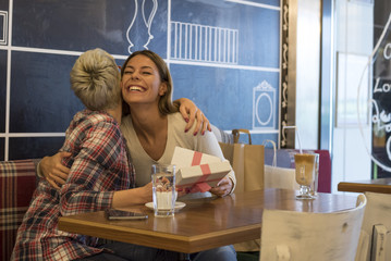 Two young women having a great time in a coffee shop while exchanging gifts