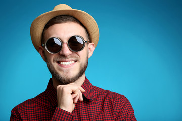 Portrait of young man with sunglasses and hat on blue background
