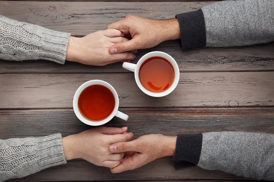 Female and male hand holding each other with cups of tea