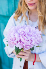 Young female hands holding beautiful tender bouquet of artificial pink peonies on mint green background