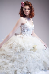 Wedding Ideas and Concepts. Young Caucasian Ginger Female Wearing Tailored Wedding Dress. Posing Against Gray Background