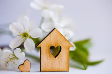 Wooden house with hole in form of heart surrounded by white flowering apricot branches on light background