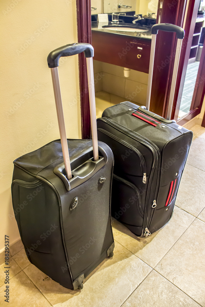 Wall mural Two black suitcases with long handles in the hotel room stand on the floor.