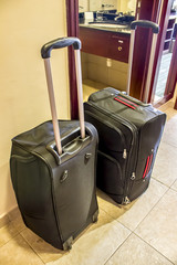 Two black suitcases with long handles in the hotel room stand on the floor.