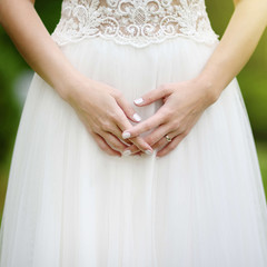 Obraz na płótnie Canvas Close-up photo of bride's hands with golden engagement ring on beautiful white wedding dress