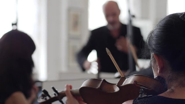 female violinist plays on fiddle in front of a musical stand on background conductor indoors