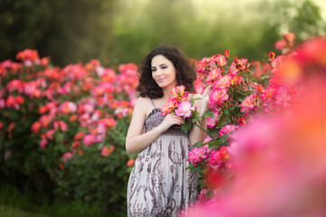 Naklejka premium Portrait of a young woman near red and pink roses bush, looking to the left