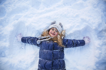 Fototapeta na wymiar Beautiful little girl wearing navy jacket and knitted hat playing in a snowy winter park. Child playing with snow in winter. Kid play and jump in snowy forest. Family vacation with child in mountains