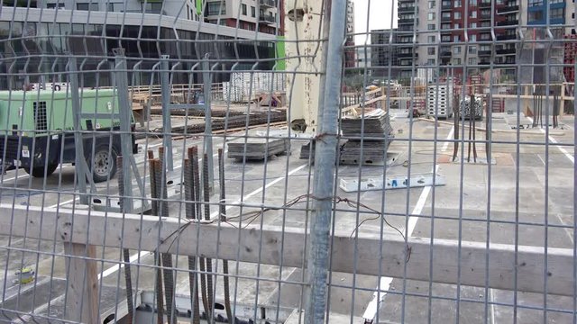 Condo, apartment building construction site ground level viewed through metal fence, barricade