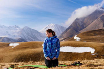 Naklejka premium active young girl in a blue jacket sits on the background of the Caucasian ridge and enjoys nature