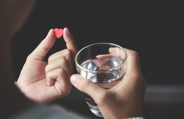 Female handsis holding red pill in heart shape and glass of water