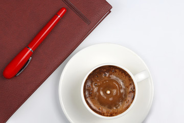 the red pen is on the Cup with black coffee and a notebook