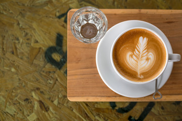 Hot Coffee Latte in white cup with water in a glass on the wooden table with space in the left side