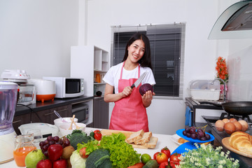 happy woman holding purple cabbage and knife in kitchen room