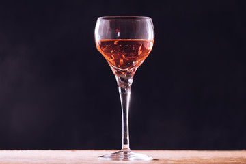 Glass of wine on the wooden table, black background.
