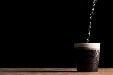 Hot water is poured into a ceramic cup on the table, black background. Free space for text