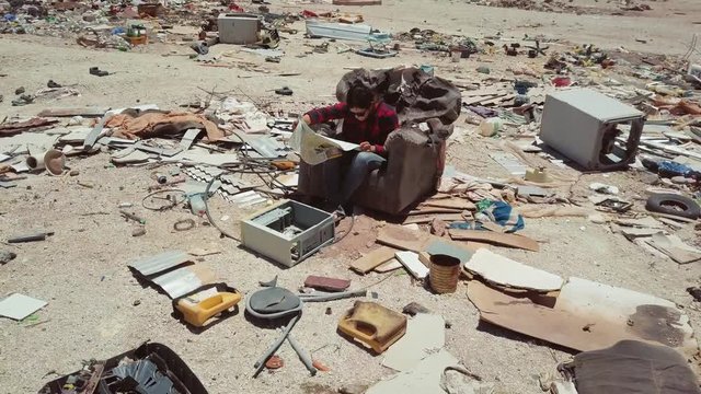 Aerial view of woman sitting in sofa surrounded by garbage, public dump in Atacama Desert. 4k	Woman surrounded by garbage