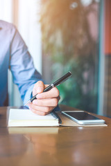 Female hand is writing on notepad with pen in office.
