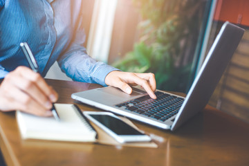 Woman hand works in a laptop computer and writes on a note pad in an office.