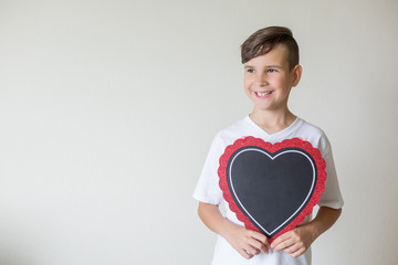 The boy holds a chalkboard in the form of a heart in his hands. Free space for your text. Beautiful...