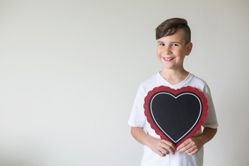The boy holds a chalkboard in the form of a heart in his hands. Free space for your text. Beautiful...