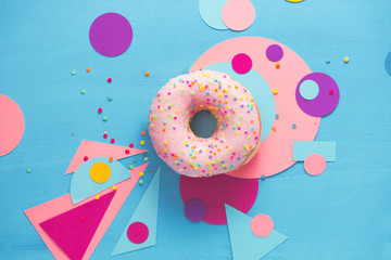 Pink glazed donut on a colorful background with geometric shapes. Color block food photography.