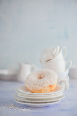 Obraz na płótnie Canvas White donut with coconut topping on a light background with porcelain cups and saucers. High key food photography. Stack of tableware.