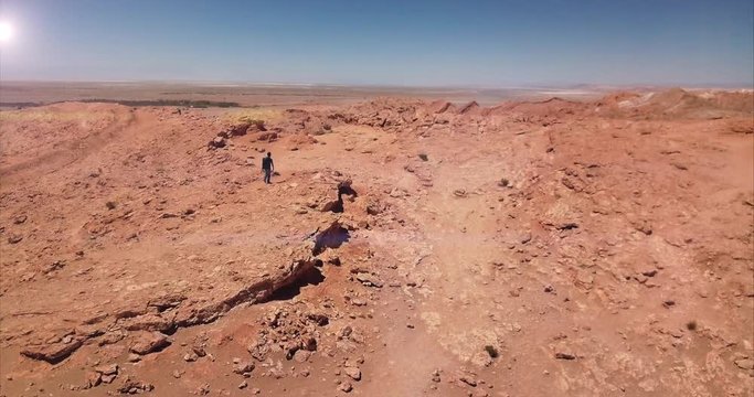 Aerial shot of male hiker carrying a backpack walking towards the edge of a rocky cliff, Atacama desert. 4k