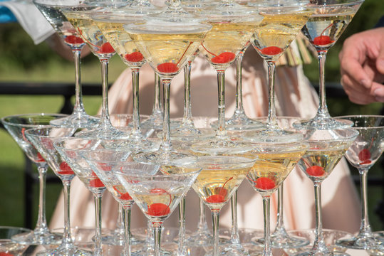 A slide of champagne. Pyramid of champagne glasses with red cherries.