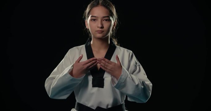 Asian beautiful girl a Taekwondo fighter performs punches in slow motion, dressed in a kimono, black background,
