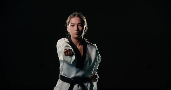 Asian beautiful girl a Taekwondo fighter performs punches in slow motion, dressed in a kimono, black background,