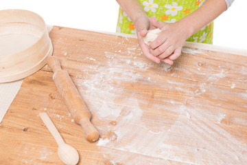 hands of a girl kneading dough and rolling out on a wooden board