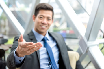 Friendly Asian businessman reaching out hand with open palm, welcome gesture