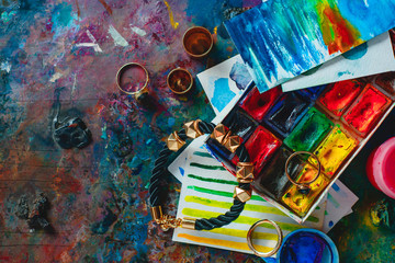 Paint brushes with sketches and woman jewelry accessories on a vivid palette. Artist tools on a dark background in creative occupation concept.