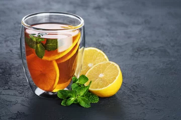 Keuken foto achterwand Thee Hete thee met munt en citroen in een glas met dubbele wanden op een donkere achtergrond.