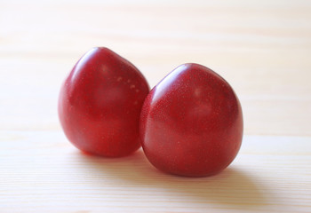 Closed up a Pair of Deep Red Color Ripe Gulf Ruby Plum Fruits Isolated on Wooden Table