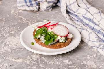 Sandwiches with cottage cheese, radish and cucumber, parsley, baking paper, white wood background