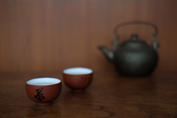 CHINESE TEA CUP WITH BLACL IRON KETTLE
Small ceramic Chinese tea cups are placed together with black iron kettle on the wood table in front of  wood wall.