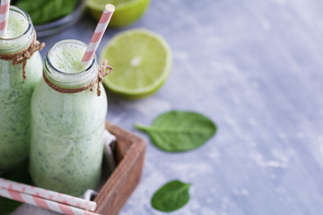 Two spinach smoothies with lime in the glass bottles with straws