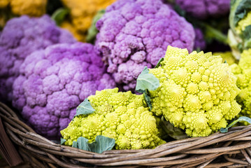 Colorful organic fresh vegetables in wooden boxes displayed at market, closeup, selective focus. Vivid green romanesco broccoli, purple and orange cauliflower at market stall, Sydney, Australia.