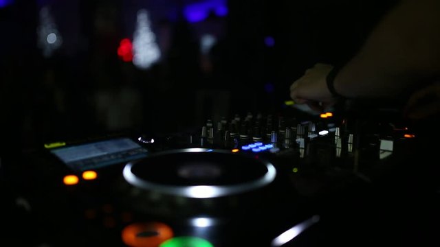 A professional DJ working in a club at a party winds a crowd of people and mixes music. DJ close-up.