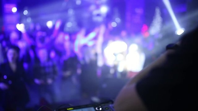 A professional DJ working in a club at a party winds a crowd of people and mixes music. DJ remote control close-up. dance floor with people in the background.