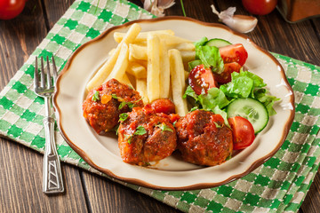 Roasted meatballs in tomato sauce with french fries and salad
