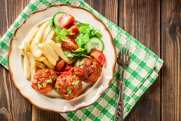 Roasted meatballs in tomato sauce with french fries and salad