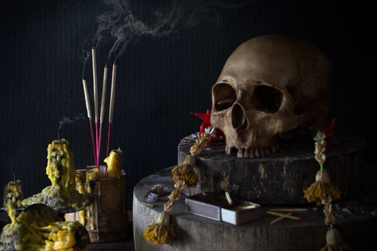 Still Life image of incense and candle with smoke and skull in room with has dim light