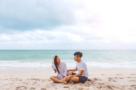 Portrait image of a lover couple sitting on the beach and looking at each other with feeling loved , the sea and blue sky background