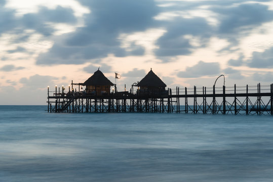 Wooden pier and thatched roofs on a tropical beach at sunrise, Zanzibar island