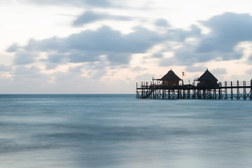 Wooden pier and thatched roofs on a tropical beach at sunrise, Zanzibar island