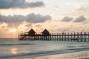 Wooden pier and thatched roofs on a tropical beach at sunrise, Zanzibar island